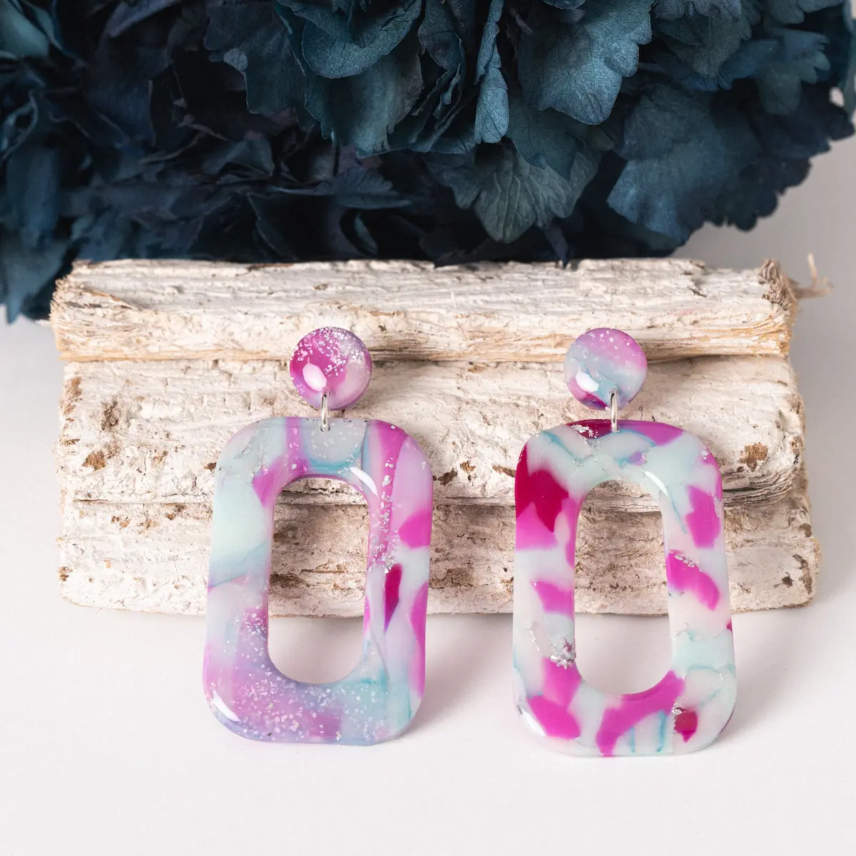 Pendientes artesanales de plata de ley 925 y arcilla polimérica. Un pequeño circulo con una pieza rectangular colgada, todo ello con un estampado en tonos rosas y azules.