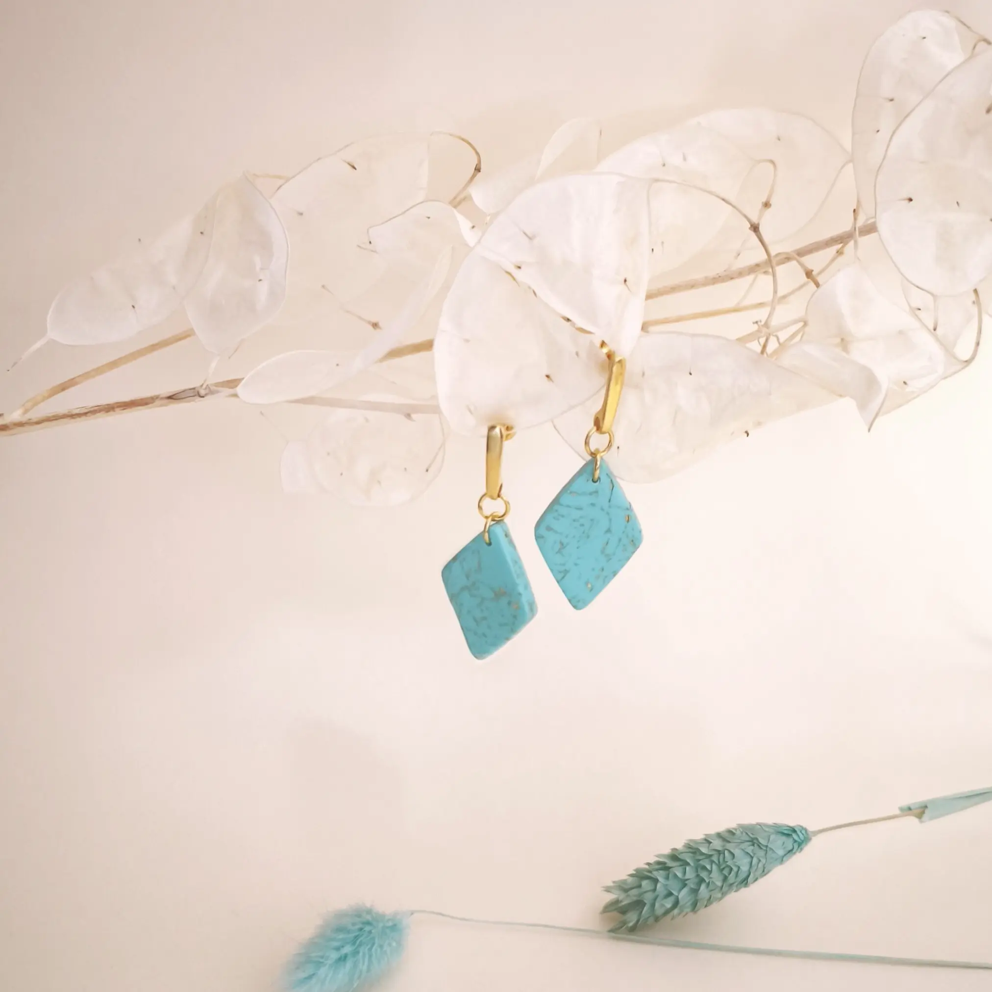 Pendientes artesanales de plata bañados en oro de 24 quilates. Con un rombo colgante en color turquesa y detalles de pan de oro.