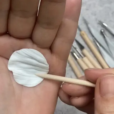 Primer plano de manos artesanas modelando la textura de un pendiente de arcilla polimérica en el taller de Pabús Bijoux, Bilbao.